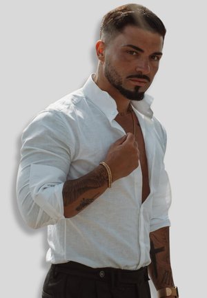 Weißes Leinenhemd mit einem entspannten Kragen, hochgerollten Ärmeln und Slim Fit. Kombiniert mit schwarzen Hosen und ergänzt durch goldenen Schmuck.