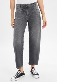 Pantalon en denim gris à coupe ample, avec deux poches avant, jambes droites et fermeture à bouton classique, associé à des baskets noires.