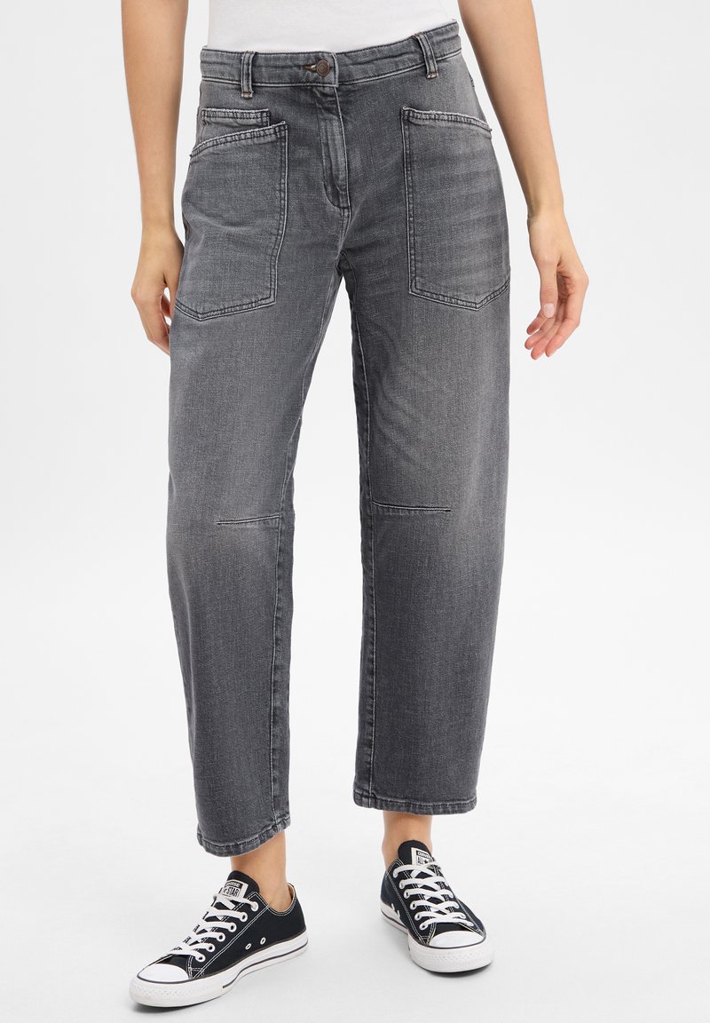 Pantalon en denim gris à coupe ample, avec deux poches avant, jambes droites et fermeture à bouton classique, associé à des baskets noires.