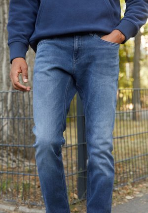 Blue denim jeans with a slim fit, light texture, and slight fading. Features a front pocket and classic waistband design.
