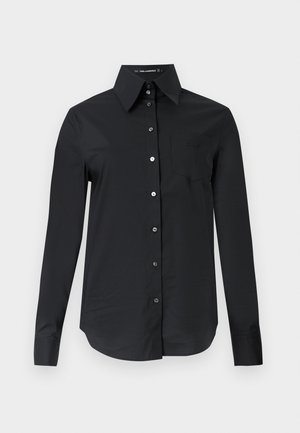 Chemise noire à manches longues avec col pointu et poche poitrine, présentée sur un fond clair uni.