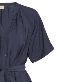 Blouse bleu marine à manches courtes avec boutons sur le devant, encolure froncée et ceinture assortie nouée à la taille.