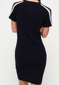 Abito in maglia blu navy a maniche corte, con strisce rosa sulle spalle. Silhouette curva, lunghezza a metà coscia, tessuto testurizzato.