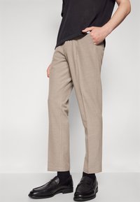 Beige op maat gemaakte broek van lichtgewicht stof, met een rechte snit, zijzakken en gecombineerd met zwarte instappers en sokken.