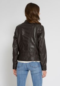 Brun läderjacka med en figurnära design, med sömsdetaljering och långa ärmar. Texturerad yta med en mjuk finish, kombinerad med blå jeans.