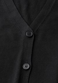 Gilet noir en tissu léger, présentant un design en V et une fermeture à bouton noir unique avec un détail de logo.