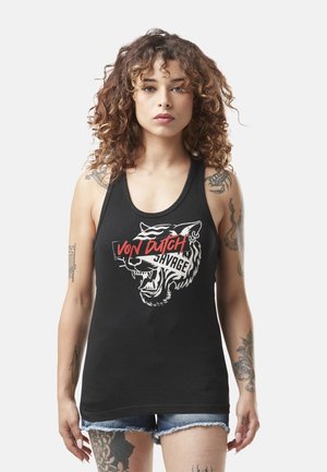 Jeune femme aux cheveux bouclés portant un haut noir sans manches avec un tigre rugissant et le texte "Von Dutch Savage", associé à un short en denim bleu.
