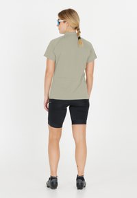 Ljust grön kortärmad topp med hög krage, kombinerad med svarta åtsittande shorts. Lättviktig tyg, slät struktur och atletisk design.