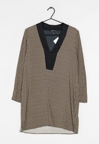 Langärmlige Tunika mit einem marineblauen Kragen und einem gemusterten Körper in Beige und Schwarz. Sie hat einen V-Ausschnitt und seitliche Schlitze am Saum.