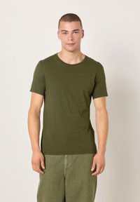Olivo zelena bombažna majica s kratkimi rokavi z okroglim izrezom in oprijetim krojem, v kombinaciji z ujemajočimi se zelenimi hlačami.