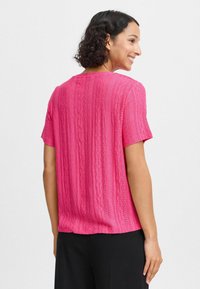 Kurzarmiger, rosa Strickoberteil mit strukturiertem Muster und Lochdetails. Lockere Passform, runder Halsausschnitt und leicht längerer Saum hinten.