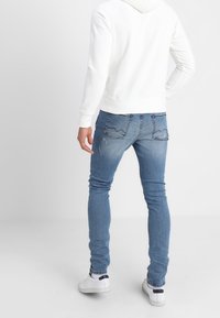 Felpa bianca con cappuccio abbinata a jeans skinny blu, con dettagli strappati e texture liscia, completata da sneaker bianche.
