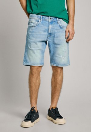 Shorts en denim bleu clair avec des détails déchirés, cinq poches et une coupe régulière. Associés à des baskets bleu foncé avec des semelles blanches.