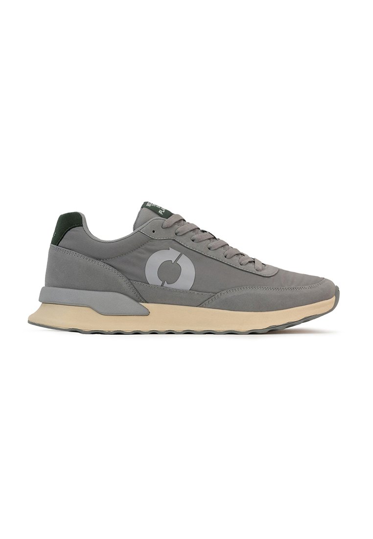 Zapatilla gris con una parte superior suave, acentos verdes y una suela de goma. Presenta un logotipo circular en el lado y un acabado texturizado en el talón.