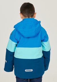 Blaue und türkisfarbene, farblich abgesetzte Jacke mit Kapuze, die eine glatte Textur und reflektierende Akzente aufweist. Logo auf dem Rücken angebracht.