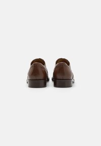 Scarpe in pelle marrone con una finitura lucida, caratterizzate da dettagli brogue e una punta arrotondata. Suola robusta con un'altezza moderata del tacco.