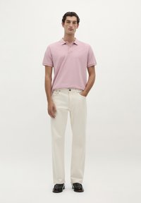 Polo shirt rose clair à manches courtes, associé à un pantalon droit écru et des chaussures noires. Tissu lisse, design minimal.