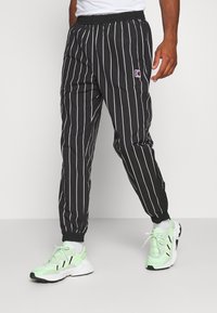 Musta-raidoitetut housut, joissa on rento istuvuus, joustava vyötärönauha ja nilkan resorit. Yhdistetty vaaleanvihreisiin urheilukenkiin.