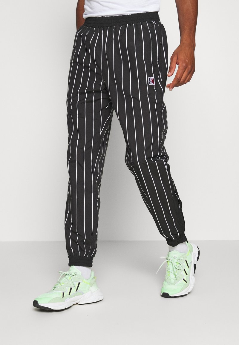 Musta-raidoitetut housut, joissa on rento istuvuus, joustava vyötärönauha ja nilkan resorit. Yhdistetty vaaleanvihreisiin urheilukenkiin.