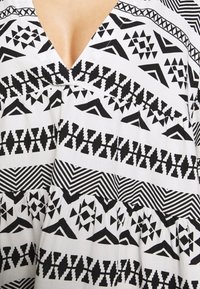 Robe à motifs noir et blanc avec des dessins géométriques, un décolleté en V profond et une texture plissée le long de l'ourlet.