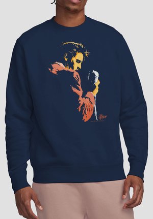 Marineblauer Sweatshirt mit buntem Motiv eines Mannes im Profil, der ein Vintage-Mikrofon hält, getragen von einer Person mit brauner Haut und rosa Hose.