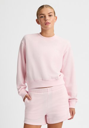 Felpa rosa chiaro con scollo rotondo, orlo a costine e logo sul petto. Abbinata a pantaloni corti rosa chiaro con vita elasticizzata.