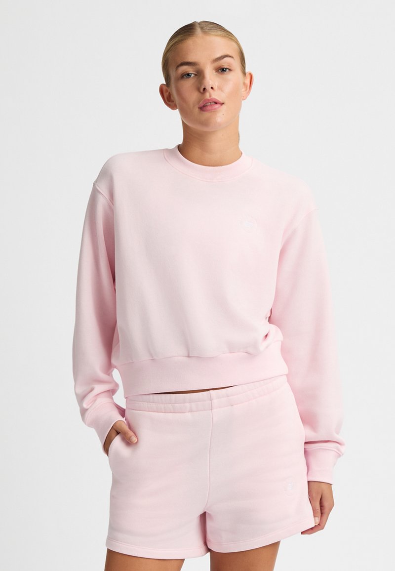 Felpa rosa chiaro con scollo rotondo, orlo a costine e logo sul petto. Abbinata a pantaloni corti rosa chiaro con vita elasticizzata.