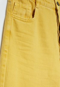 Gul denimkjol med en framficka, texturerad tyg och knappstängning, med synlig sömnadsdetaljering längskanterna.
