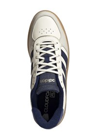 White and navy sneaker with a textured upper, three navy stripes, and a beige rubber sole. Features a padded tongue and logo detail.