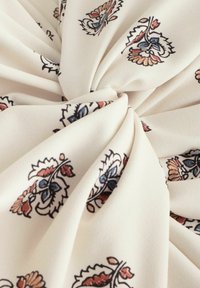 Tissu en coton avec un fond crème et des motifs floraux complexes en bleu, rouge et marron. Texture douce avec des détails froncés.