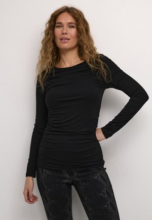 Haut noir à manches longues avec un design ajusté et une texture froncée. Associé à un legging noir avec un motif de peau de serpent.