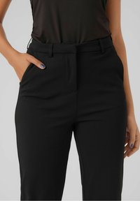 Czarne dopasowane spodnie o gładkiej fakturze, prostym kroju, bocznych kieszeniach i subtelnym przednim załamaniu, zaprojektowane dla dopasowanego wyglądu.