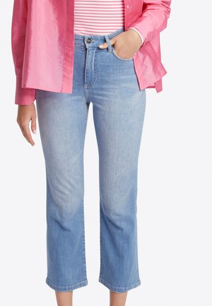 Hellblaue, kürzere Jeans mit hohem Bund, geradem Bein und dezentem Verblassen. Kombiniert mit einem gestreiften Hemd und einer rosa, glänzenden Bluse mit Knöpfen.