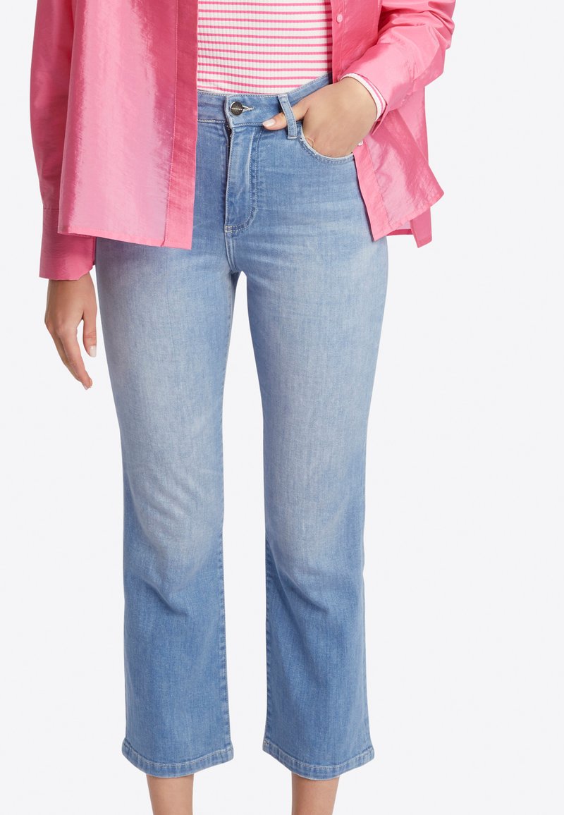 Pantalones vaqueros cortos de color azul claro con una cintura alta, pierna recta y un desvanecimiento sutil. Combinados con una camisa a rayas y una chaqueta de botones rosa y brillante.