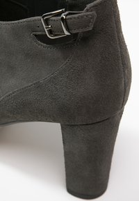 Bottine en daim gris foncé avec un talon bloc et une sangle à boucle argentée près du bord supérieur.