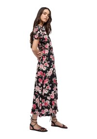 Abito nero floreale con fiori rosa e bianchi, caratterizzato da maniche a volant corte e una gonna fluida. Indossato con sandali neri con cinturini.