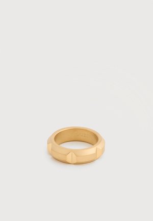 Gold-colored metal ring with geometric raised details and "GUESS" engraved inside, set against a plain light background.