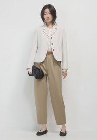 Blazer beige clair à deux boutons, blouse crème, ceinture marron, pantalon beige ample et pochette noire. Comprend des chaussures noires plates et un design simple.