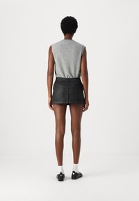 Šedý bezrukávový pletený top v kombinaci s černou džínovou mini sukní. Oblečení má slim fit a zadní kapsy. Černé boty s bílými ponožkami.