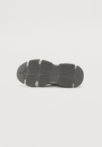 Suela de zapatilla deportiva gris con una superficie de goma texturizada, patrones de tracción y acentos en gris claro. Punta redondeada y talón reforzado.