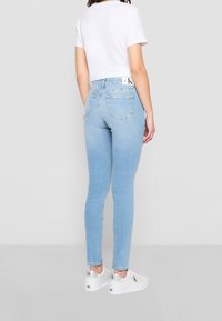 Tunna ljusblå jeans med hög midja, med bakfickor och en vit linning med varumärke, i kombination med vita sneakers.