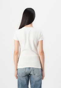 Hvid kortærmet T-shirt med slim fit og rund halsudskæring. Stoffet har en glat tekstur. Kombineret med blå denim jeans.