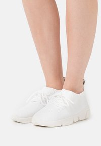 Bílé pletené tenisky s nízkým střihem, šněrováním, texturovaným povrchem a odolnou gumovou podrážkou.