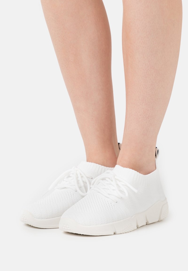 Bílé pletené tenisky s nízkým střihem, šněrováním, texturovaným povrchem a odolnou gumovou podrážkou.
