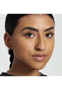 Gros plan d'un visage avec une peau lisse, des cheveux tressés, des yeux marron foncé et des sourcils bien dessinés. Bijoux minimalistes : boucles d'oreilles créoles et puces.