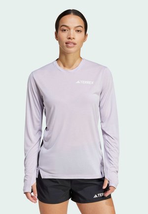 Licht paarse lange mouwen sportshirt met een ronde hals en zijpanelen van gaas, met een witte "TERREX" logo. Gecombineerd met zwarte shorts.