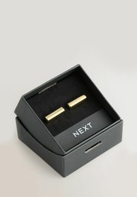 Gold-tone cufflinks with a smooth, rectangular design, displayed in a black box with a velvet interior and "NEXT" label.
