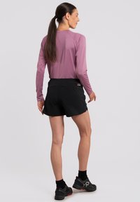 Maglietta atletica rosa a maniche lunghe abbinata a pantaloni corti neri. Il materiale sembra leggero. Calzature nere con dettagli rossi completano il look.