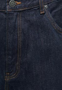 Jean en denim bleu foncé en gros plan montrant un bouton en métal avec le texte "ONLY & SONS" et des détails de couture orange autour des poches et de la ceinture.