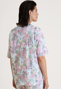 Camicetta a maniche corte realizzata in tessuto leggero, con un motivo floreale e architettonico in tonalità pastello di rosa, verde e blu.